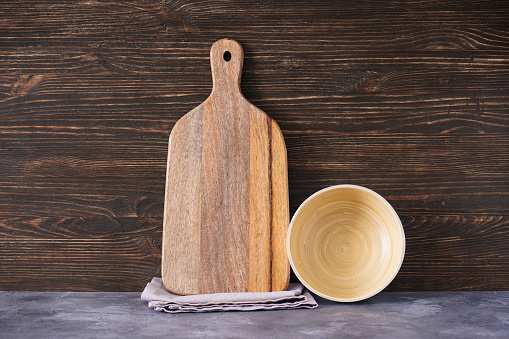 Wooden cutting board and kitchen utensils on a wooden background, space for text.