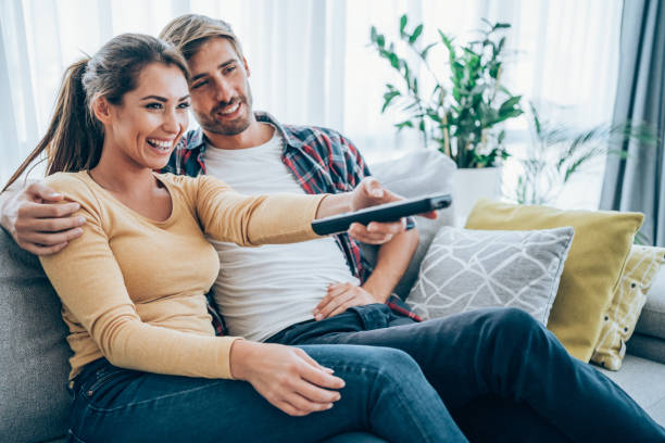 Cute young couple cuddling while watching tv. Beautiful young happy couple sitting on a couch at home and watching tv. couple isolated wife husband stock pictures, royalty-free photos & images