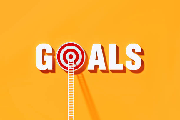 istock White Ladders Leaning on Goals Written  Bull's Eye Target on Yellow Wall 1290371152