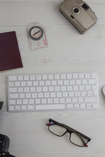 workspace with a white keyboard, glasses, notebook, compass, old camera. On a white wooden textured desk