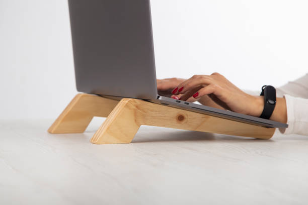 hand using a laptop, the computer is on a wooden stand for better ergonomics, lifestyle stock photo