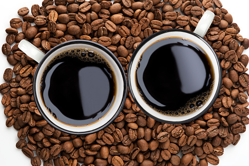 a cup of black coffee on a white background and coffee beans in the shape of a heart