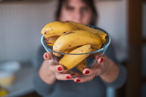 Woman holding a full of banana bowl to the camera