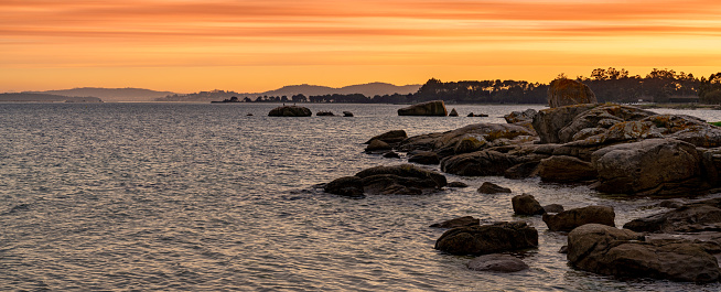 Panorama view of beautiful and wild red granite boulder coastline on the Atlanic at sunset with mountainous shore behind