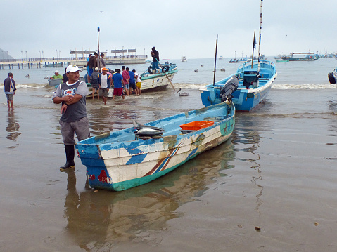 Puerto Lopez, Ecuador - July 17, 2017: Fishing boats in the cloudy morning along a beach shore in a port of Puerto Lopez, Manabi province. Fisherman sells his catсh