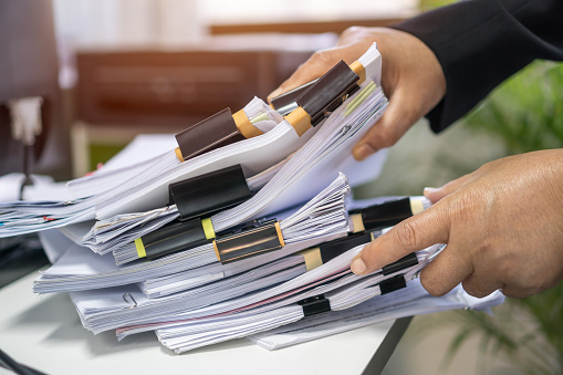Office workers arranging stacks of lot paperwork files for searching infomation unfinished documents about pile audit form on desk offices and investigate financial doc messy in busy workload