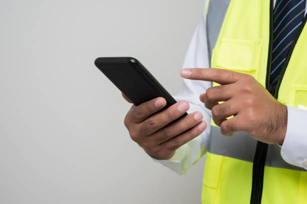 istock Close up male hands engineer holding mobile phone. Worker using smartphone standing on isolated white background. 1290419429