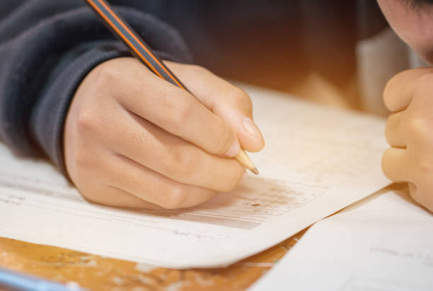 istock Students hands taking exams, writing examination room with holding pencil on optical form of standardized test with answers and english paper sheet on row desk chair doing final exam in classroom. 1290426785