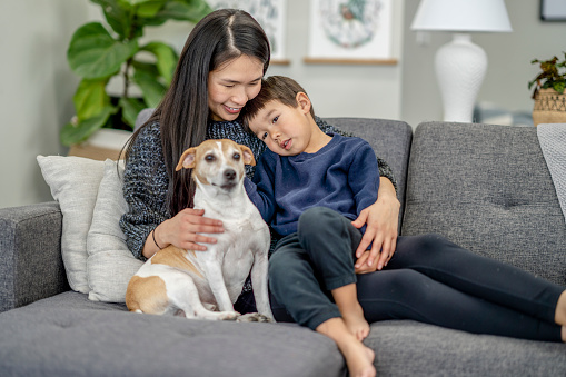 Young Asian mother sitting with her son on the couch with their dog enjoying some quality time together.
