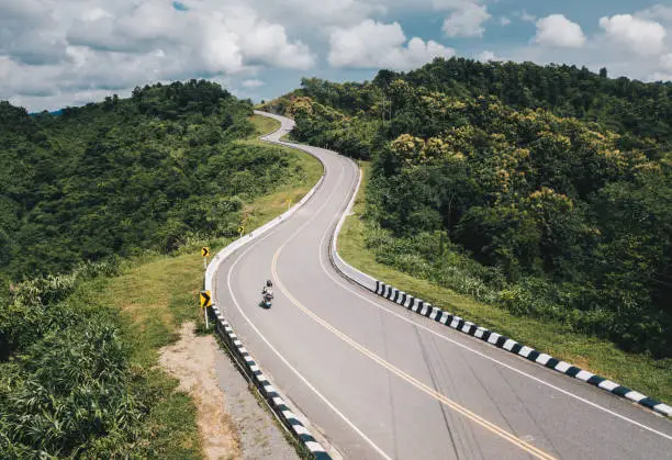 Photo of Aerial view of tourist riding a motorcycle on beautiful steep curved road (look like number 3) on the high mountain in Nan province, Thailand.
