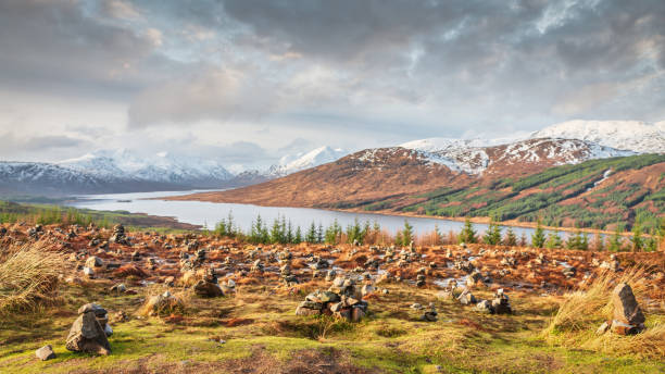 Loch Loyne Cairns Scottish Highlands Winter Panorama Scotland UK Loch Loyne Scottish Highlands Winter Panorama. Snowcapped Scottland Mountains under beautiful sunny cloudscape. Scottish Rock Cairns - Rock Stacks in the foreground of the Panorama. Winter Landscape Panorama Northwest Highlands Loch Loyne, Scotland, United Kingdom, Europe. fort augustus stock pictures, royalty-free photos & images