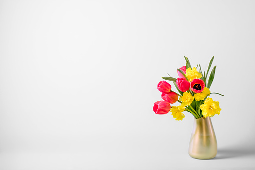 Spring bouquet of yellow buttercups, white daffodils and tulips, bouquet of flowers on the table near the wall, home decoration with flowers