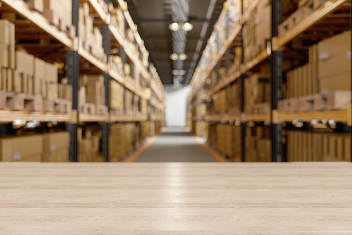 Wood Table In The Warehouse With Blur Background And Cardboard Boxes On The Rack.