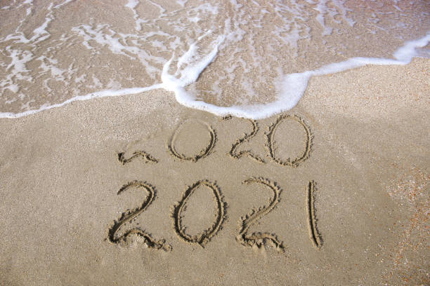 istock 2020, 2021 years written on sandy beach sea. Wave washes away 2020. 1290450613