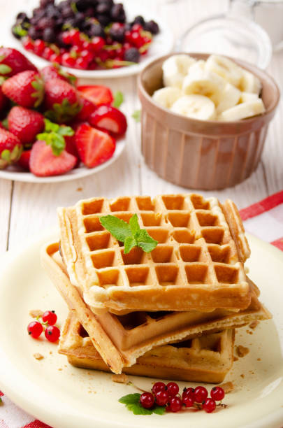 istock Stack of three belgian waffles on white kitchen table with strawberries bananas and red currant 1290451305
