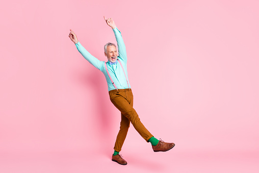 Full length body size photo of cheerful man dancing keeping hands fingers up wearing bowtie suspenders isolated on pink color background.