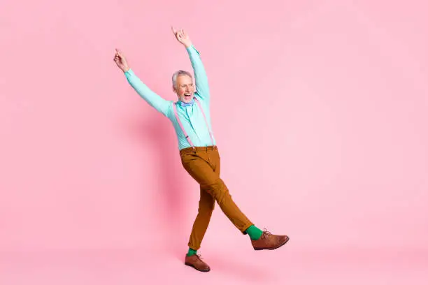 Photo of Full length body size photo of cheerful man dancing keeping hands fingers up wearing bowtie suspenders isolated on pink color background