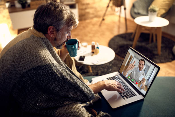 istock Man wrapped in blanket drinking tea while having video call with a colleague in the evening at home. 1290458114