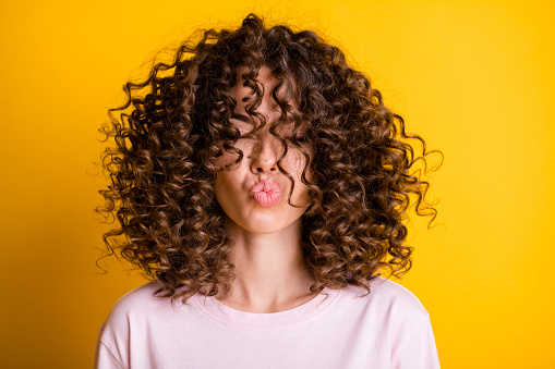 Headshot of girl with curly hairstyle wearing t-shirt send air kiss pouted lips isolated on vivid yellow color background.