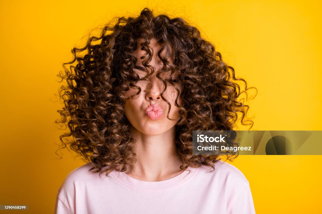 Headshot of girl with curly hairstyle wearing t-shirt send air kiss pouted lips isolated on vivid yellow color background Headshot of girl with curly hairstyle wearing t-shirt send air kiss pouted lips isolated on vivid yellow color background. Curly Hair Stock Photo