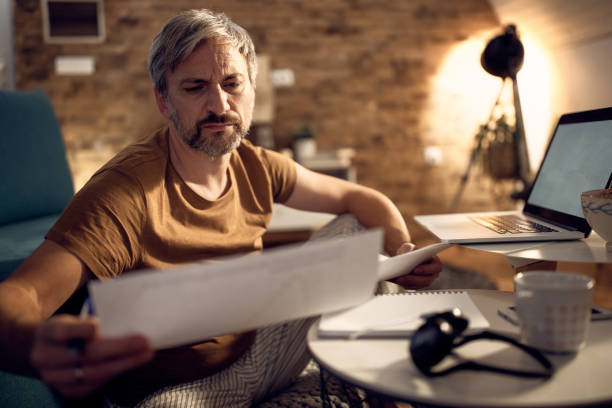 istock Businessman in pajamas analyzing paperwork while working late in the evening at home. 1290458307