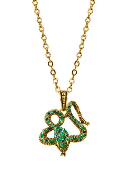 Gold pendant in the shape of a snake with green gems hanging on a chain on white background