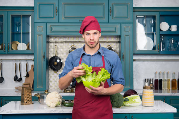 istock Man chef in red hat, apron hold green salad leaves 1290459278