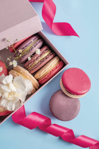 istock Multicolored macarons in a pink box on a blue background. Birthday present, sweet biscuits. Copy space 1290461974