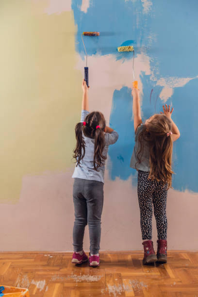 istock Two little girls reaching up while painting the wall 1290465580