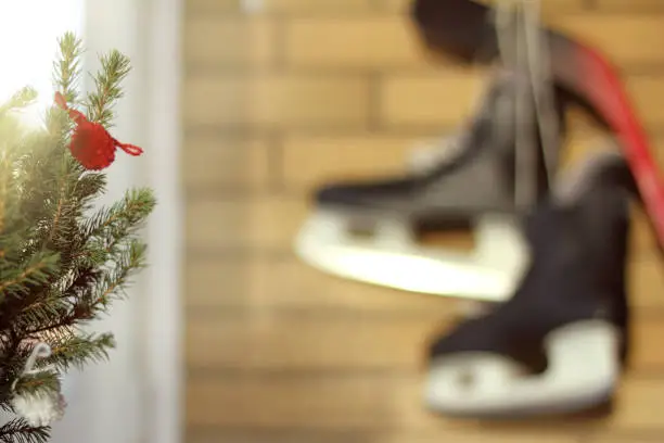 festive tree on a blurred background with skates and a hockey stick hanging on the wall by the window