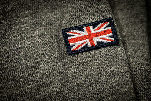 Extreme closeup of a clothing label with the UK flag (Union Jack Flag) sewn on a grey fabric. Made in Kingdom, concept.