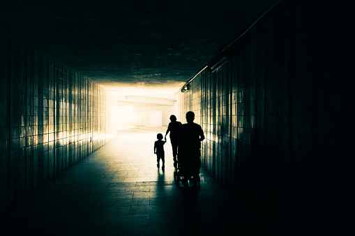 Prague, Czech Republic - August 7, 2017: Silhouette of happy family with children. Mother and daughter holding hands. Father and baby in stroller going behind. People are walking along the underground tunnel. Light at end of long corridor.