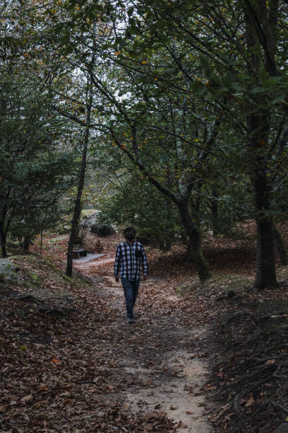 istock Young man walking though a forest with brown colored leaves around him wearing a face mask 1290473871
