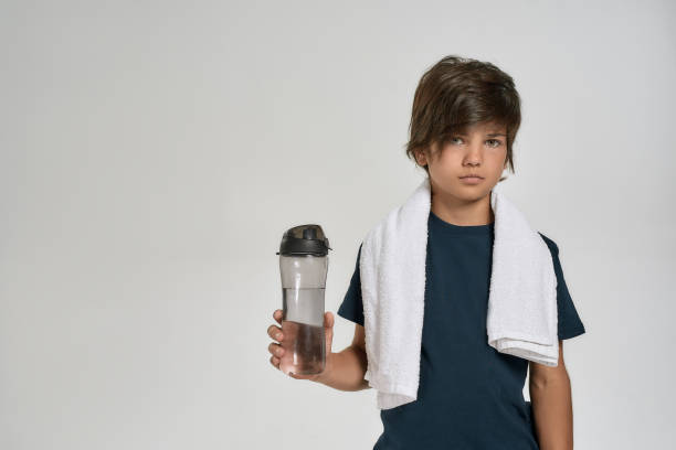 little sportive boy child in sportswear looking at camera, holding a water bottle while standing with white towel around his neck isolated over white background - small gymnastics athlete action imagens e fotografias de stock