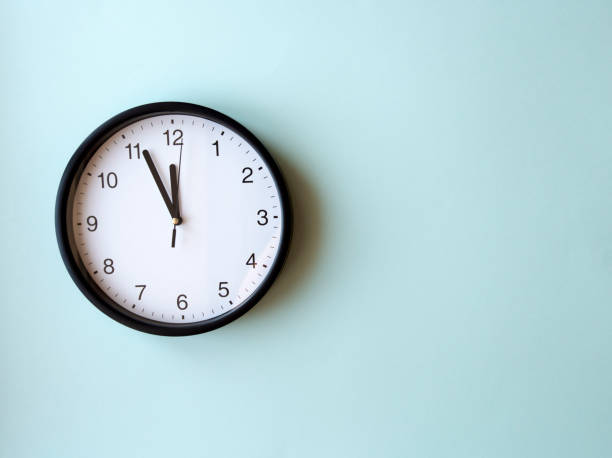 istock Round wall clock on blue surface showing 12 oclock, layout, top view, place for text 1290477349