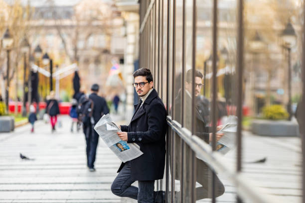 istock Reading the latest news. Confident young man in full suit reading newspaper while standing outdoors with cityscape in the background 1290479766