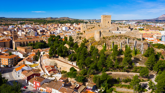 Scenic aerial view of residential areas in small Spanish town of Almansa with dominating medieval walled Castle on hilltop on sunny fall day