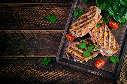 Grilled sandwich panini with ham, tomato, cheese and spinach. Delicious breakfast or snack. Top view, copy space, overhead