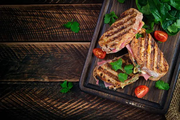 Grilled sandwich panini with ham, tomato, cheese and spinach. Delicious breakfast or snack. Top view, copy space, overhead