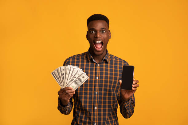 istock Surprised black guy holding smartphone with blank screen and dollar cash 1290488177