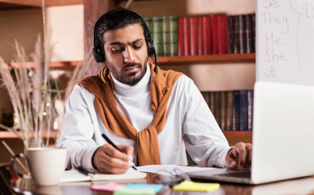 istock Arab Teacher Sitting At Laptop Taking Notes At Home 1290488249
