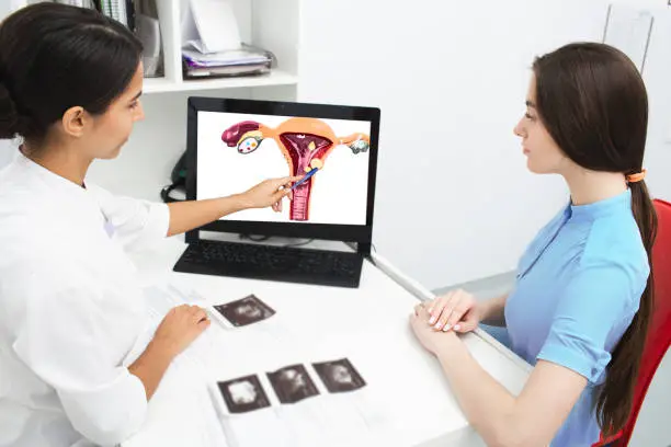 Gynecology, consultation. Gynecologist explains to a woman about a disease of the uterus, showing an endometrial polyp on her laptop