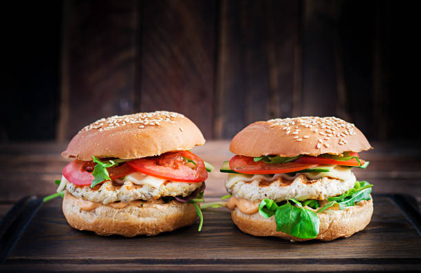 большой сэндвич - гамбургер бургер с мясом индейки, помидорами, огурцами и салатом. - turkey burger стоковые фото и изображения