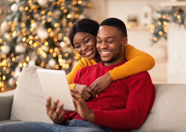 glücklich millennial afrikanischen amerikanischen kerl und dame umarmung und schauen sie auf tablet und machen videoanruf - christmas shopping internet family stock-fotos und bilder