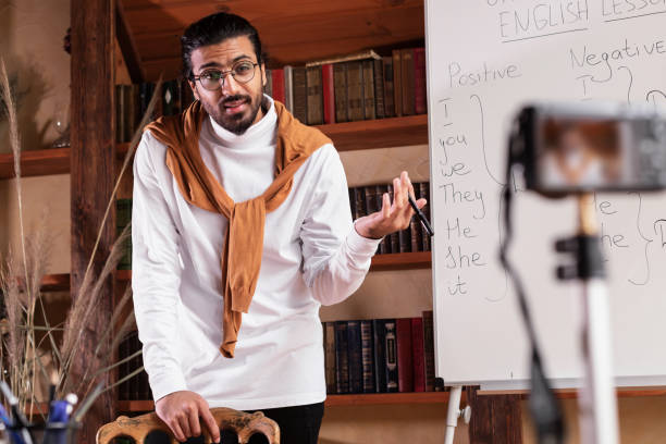 istock Teacher Man Making Video Lecture Teaching English Online Standing Indoors 1290490814