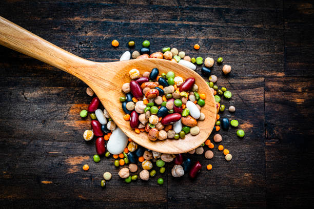 gemischte getrocknete hülsenfrüchte in einem holzlöffel schuss von oben auf dunklen tisch - soybean fava bean broad bean bean stock-fotos und bilder