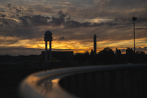 Sunset at Berlin Tempelhof Airport. Reflection of flight tower and buildings in metal railing. Clouds sky dramatic dusk beautiful colors outdoor nature freedom party beer drinking flying urban city