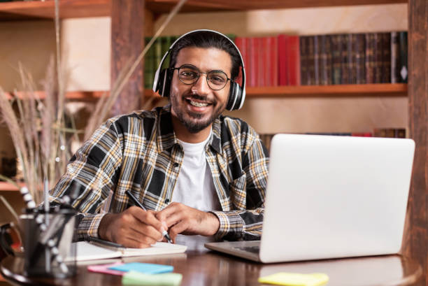 istock Indian Student Guy Posing At Laptop Learning Online In Library 1290493925