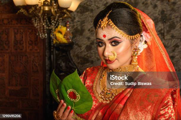 Portrait Of Very Beautiful Indian Bride Holding Betel Leaf Bengali Bride In Traditional Wedding Saree With Makeup And Heavy Jewellery In Studio Lighting Indoor Stock Photo - Download Image Now