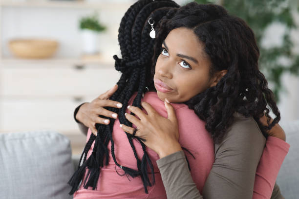 Irritated black lady hugging her girlfriend, fake friendship Irritated black lady hugging her girlfriend with annoyed face expression, fake friendship concept. Two african american women embracing, crying lady looking for support, copy space envy stock pictures, royalty-free photos & images